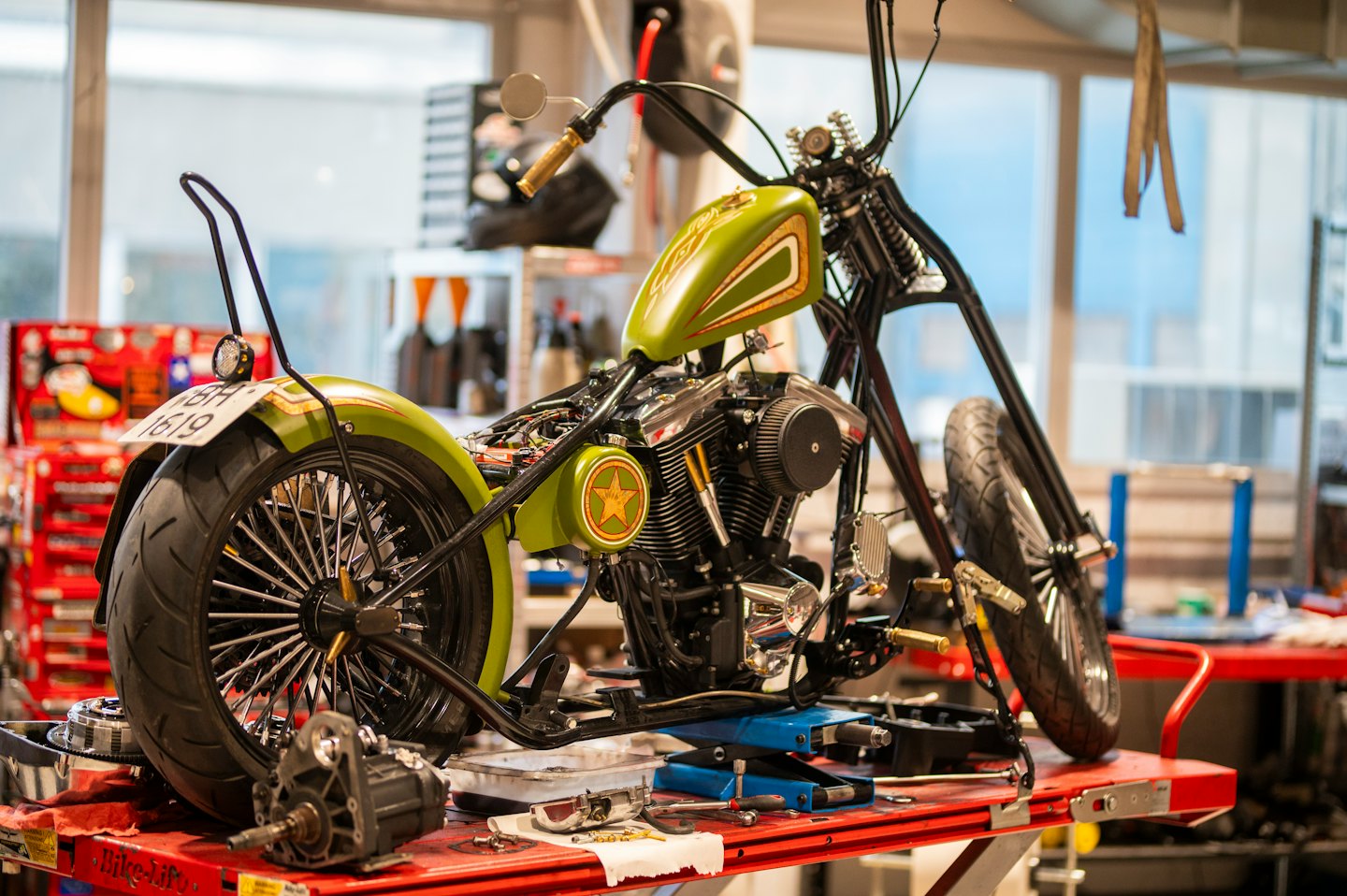 Grünes und schwarzes Motorrad wird auf einer Hebebühne in einer Werkstatt repariert.